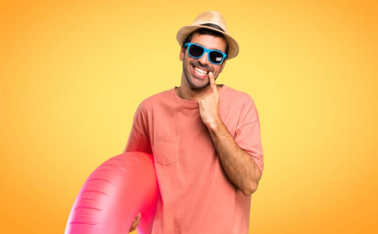 Man met hoed, zonnebril en opblaasbare ring op gele achtergrond.